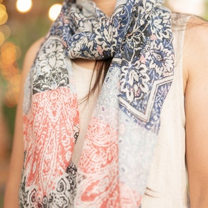 May include: A woman wearing a white sleeveless top with a colorful patterned scarf around her neck. The scarf has a paisley design with shades of blue, red, and white.