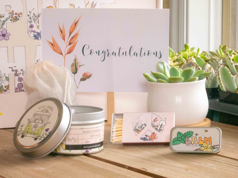 K&ouml;nnte beinhalten: Ein Geschenkset mit einer Kerze, Streichh&ouml;lzern, Lippenbalsam und einer kleinen Tasche. Die Kerze befindet sich in einer silbernen Dose mit einer Illustration eines gr&uuml;nen und gelben Lieferwagens und dem Text "Pure Chill". Die Streichh&ouml;lzer sind in einer rosa und wei&szlig;en Schachtel mit einem Blumendesign. Der Lippenbalsam befindet sich in einer silbernen Dose mit einem gr&uuml;nen Blattdesign und dem Text "BALM". Die Tasche ist wei&szlig; und aus Naturstoff.