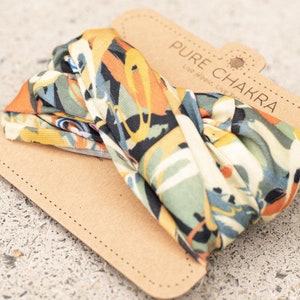 May include: A colorful headband with a floral pattern in shades of orange, green, blue, and yellow. The headband is packaged on a brown card with the text "PURE CHAKRA Live Hippie Live Free".