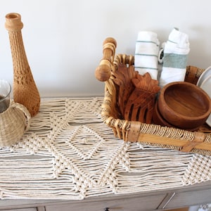 May include: A woven table runner with a geometric pattern, a wooden vase, two woven baskets, a wicker basket with wooden bowls, a pineapple-shaped wooden carving, and two white plates.