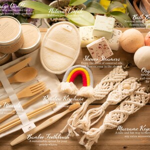May include: A collection of self-care and bath products, including a massage candle, bath bombs, shower steamers, organic soap, a loofah, bamboo utensils, a bamboo toothbrush, and macrame keychains. The products are arranged on a wooden surface with a rainbow keychain in the center.