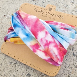 May include: A colorful tie-dye headband in shades of pink, blue, yellow, and orange. The headband is displayed on a brown cardboard tag with the text "PURE CHAKRA" and the slogan "Live Hippie. Live Free."