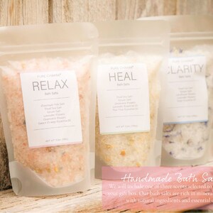 May include: Three clear plastic pouches filled with bath salts. The pouches are labeled "Relax", "Heal", and "Clarity". The bath salts are a mix of pink, white, and blue crystals. The pouches are sitting on a wooden surface. Handmade Bath Salts. We will include one of three scents selected to best match your gift box. Our bath salts are rich in minerals and made with natural ingredients and essential oils.