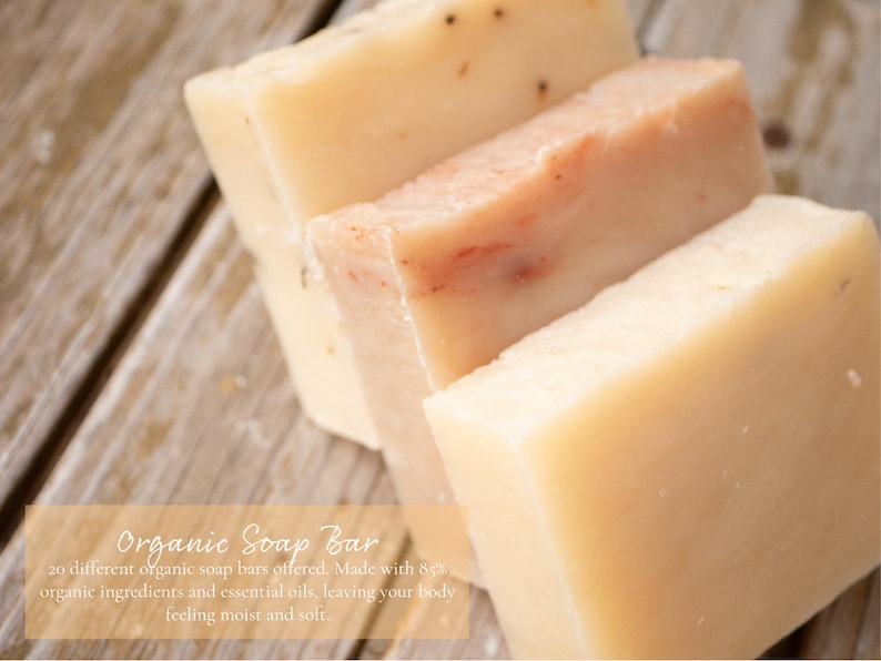 May include: Four bars of organic soap, two are a light beige color and two are a light peach color. The soap bars are stacked on top of each other on a wooden surface. The text "Organic Soap Bar" is written in a light brown font on a light orange background.