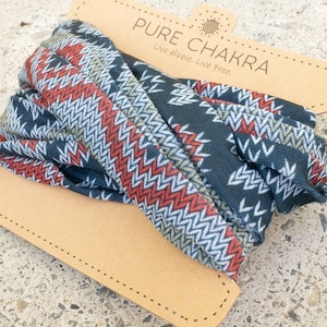 May include: A rolled-up headband with a geometric pattern in navy blue, red, white, and tan. The headband is on a tan cardboard tag with the text "PURE CHAKRA" and "Live Hippie. Live Free."
