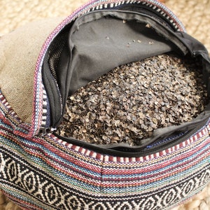 May include: A colorful patterned round cushion filled with buckwheat hulls. The cushion is open and the buckwheat hulls are visible.