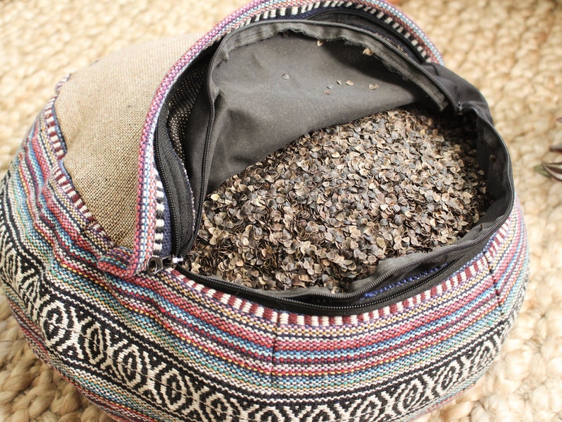 May include: A colorful patterned round cushion filled with buckwheat hulls. The cushion is open and the buckwheat hulls are visible.