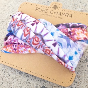 May include: A white fabric headband with a colorful, abstract pattern. The headband is folded and displayed on a brown cardboard tag with the text "PURE CHAKRA Live Hippie. Live Free."