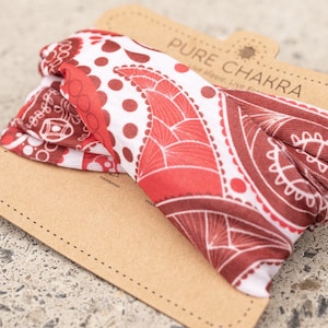 May include: A red and white paisley patterned headband with the text "PURE CHAKRA" on the packaging. The headband is made of a soft, stretchy fabric and is designed to be worn as a hair accessory.