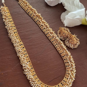 Può includere: Una collana d'oro con perle bianche e orecchini abbinati. La collana ha un design floreale ed è composta da più file di perle.