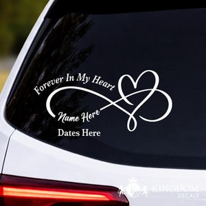 May include: White decal with the text "Forever In My Heart," "Name Here," and "Dates Here." The design features a heart intertwined with an infinity symbol. The decal is displayed on a car window.
