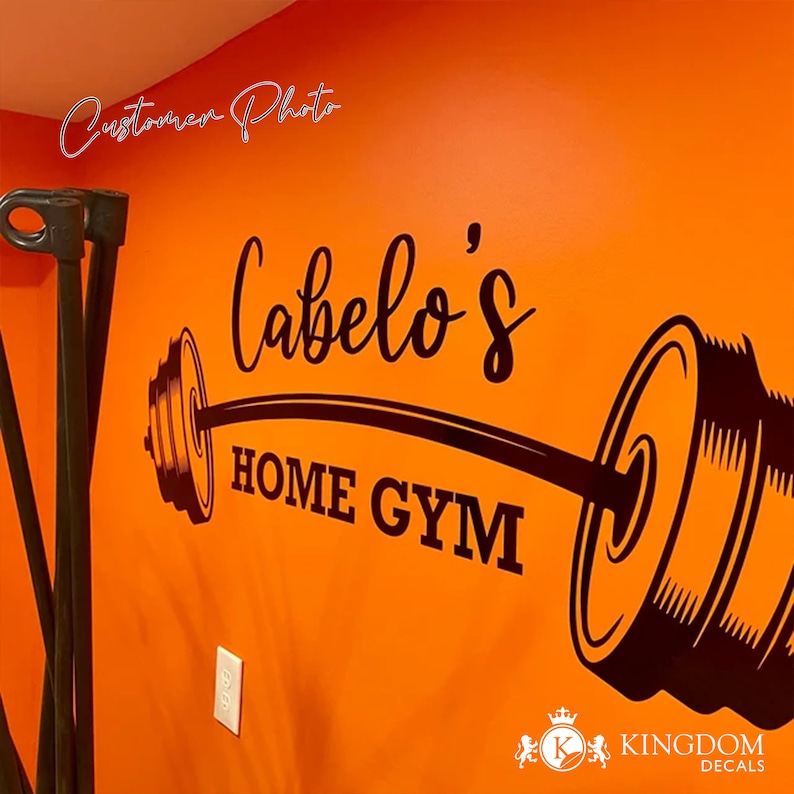 May include: Black and white vinyl decal of a barbell with weights on each end. The decal says "Cabelo's Home Gym" in a cursive font.