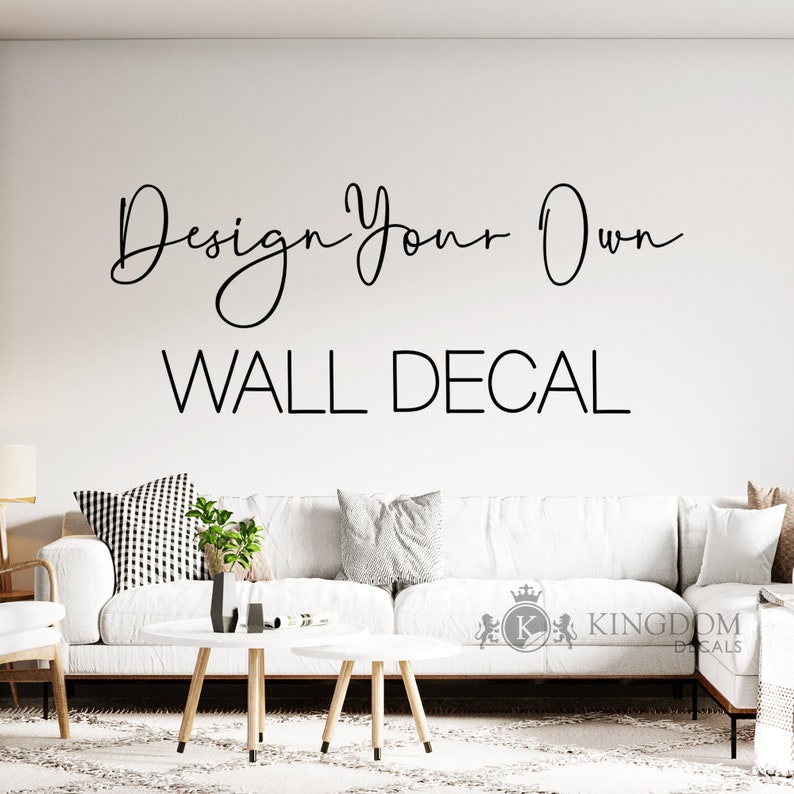 May include: A white couch with pillows in a living room setting. The wall behind the couch has a black vinyl decal that reads "Design Your Own WALL DECAL".