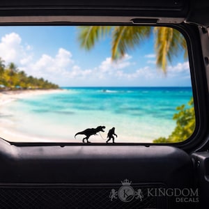 Puede incluir: Calcoman&iacute;a de vinilo negro con la silueta de un T-Rex con correa, guiado por una figura de Bigfoot. El fondo muestra una escena de playa tropical a trav&eacute;s de la ventana de un veh&iacute;culo. Incluye el texto "KINGDOM DECALS".