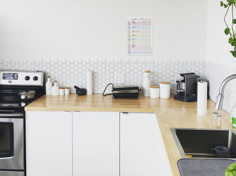 May include: A modern kitchen with white cabinets, a stainless steel stove, and a wood countertop. There are various kitchen appliances on the counter, including a coffee maker, a panini press, and a mortar and pestle. The backsplash is white hexagonal tiles.