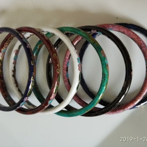 May include: Seven colorful enamel bangle bracelets with floral designs. The bracelets are in shades of blue, green, white, pink, and brown.