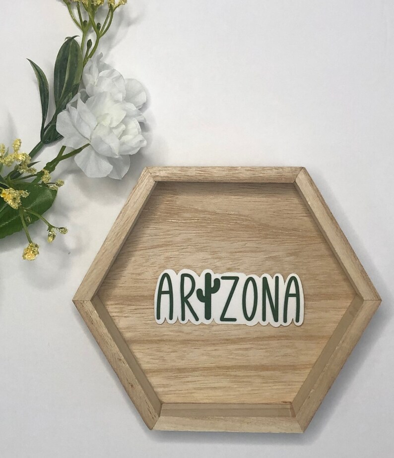 May include: A green and white sticker with the word "ARIZONA" and a cactus graphic on a wooden hexagonal tray.