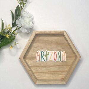 May include: A wooden hexagonal tray with the word "ARIZONA" in colorful letters with a green cactus in the middle of the word.