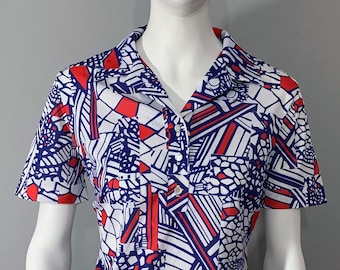 May include: A white short-sleeved shirt with a geometric pattern in red, blue, and white. The shirt has a collar and a button closure.