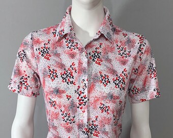 May include: A white button-down shirt with a short sleeve and a red, black, and gray abstract print.