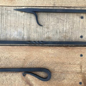 May include: Three black metal fireplace tools with a wooden handle. The tools are a poker, a shovel, and a tongs. The tools are on a wooden surface.