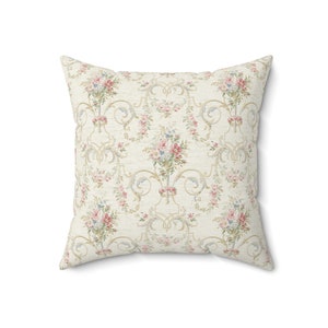 May include: A cream-coloured pillow with a floral pattern featuring pink and white roses, green leaves, and a gold scroll design.