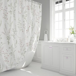 May include: White shower curtain with a delicate floral pattern in shades of pink and green. The curtain hangs in front of a white bathtub in a bright, clean bathroom setting. The floral design adds a touch of nature to the bathroom.