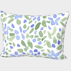 May include: A white pillow with a blue and green watercolor floral pattern. The pillow is rectangular and has a white background.