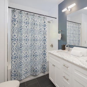 May include: A white and blue patterned shower curtain with a geometric design. The shower curtain is hanging in a bathroom with a white vanity and a white toilet.