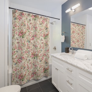Puede incluir: Una cortina de ducha blanca con un patrón floral en tonos de rosa, rojo y azul. La cortina está colgada en un baño con un tocador blanco y una encimera de mármol.