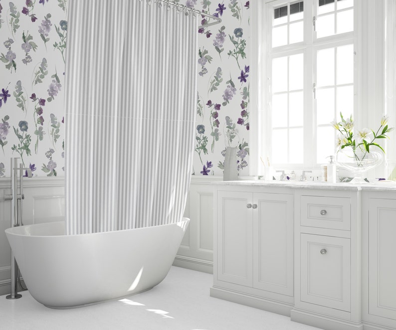 May include: A bright, white bathroom with a freestanding tub and a striped shower curtain. The walls feature floral wallpaper in shades of purple and green. A white vanity with a marble countertop and a large window complete the space.