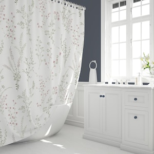 May include: A white shower curtain with a floral pattern of pink and green flowers and leaves. The shower curtain is hanging in a bathroom with a white bathtub and white cabinets.