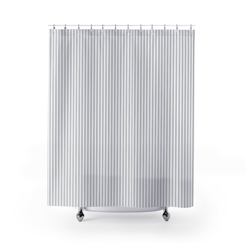 May include: A grey and white striped shower curtain suspended from a metal rail with silver hooks. The curtain features vertical stripes of varying widths, offering a classic, clean aesthetic. The curtain hangs in front of a white shower base.