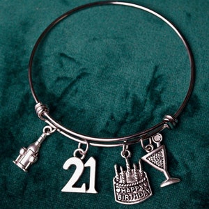 May include: A silver charm bracelet with a 21 charm, a champagne glass charm, a bottle of champagne charm, and a cake charm that says "Happy Birthday".