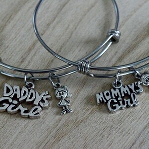 May include: Two silver bangle bracelets with charms. One charm says "Daddy's Girl" and the other says "Mommy's Girl". Both charms have a small girl figure.