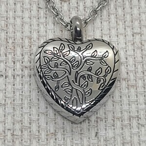 May include: A silver heart-shaped pendant necklace with a tree of life design. The pendant is detailed with a tree trunk and branches with leaves.