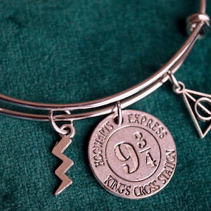May include: A silver charm bracelet with charms featuring the Hogwarts Express, Platform 9 3/4, a lightning bolt, and the Deathly Hallows symbol.