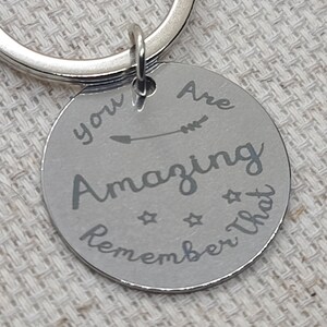 May include: Silver keychain with a round charm that says "You Are Amazing Remember That" with an arrow pointing to the right.