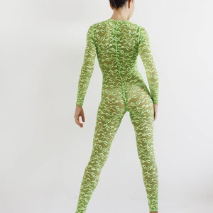 Könnte beinhalten: Ein durchsichtiger, limegrüner Jumpsuit mit floralem Spitzenmuster. Der Jumpsuit hat lange Ärmel und einen hohen Ausschnitt.