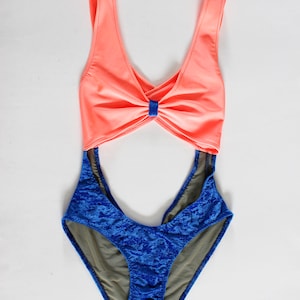 Puede incluir: Un traje de baño de color coral y azul con un diseño cruzado en la parte delantera y un panel de malla en la parte posterior.