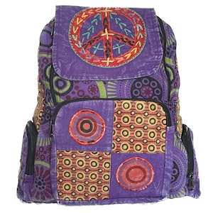 May include: Purple canvas backpack with a peace sign embroidered on the front flap. The backpack has a patchwork design with circles and other geometric shapes in shades of red, orange, yellow, and green.