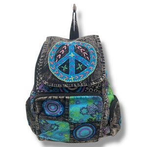 May include: A black and blue patchwork backpack with a large embroidered peace sign on the front. The backpack has a variety of colorful patterns, including circles, flowers, and paisley.