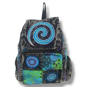 May include: Black backpack with a spiral design and patchwork details. The backpack features a large blue spiral on the flap and colorful patches with floral and geometric patterns. It has a zippered front pocket and side pockets.