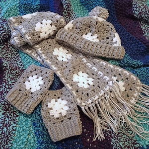 May include: A crocheted winter set in brown and white with a hat, scarf, and mittens. The hat has a white pompom on top. The scarf has fringe on the ends. The mittens have a white snowflake design.