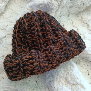 May include: A brown and black knitted beanie hat with a textured stitch pattern.