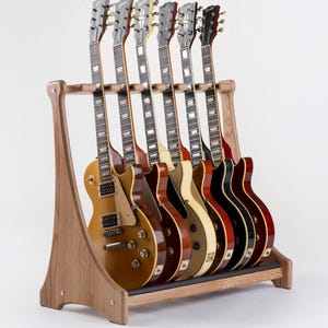 Könnte beinhalten: Ein Gitarrenständer aus Holz mit sieben E-Gitarren. Die Gitarren sind in verschiedenen Farben gehalten, darunter Gold, Creme, Schwarz und Rot. Der Ständer ist aus hellem Holz gefertigt und hat ein schlichtes, elegantes Design.