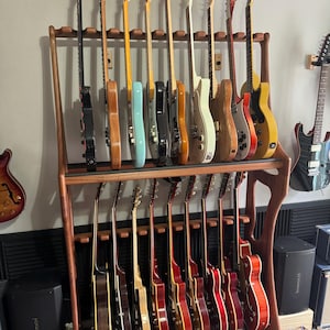 May include: A wooden guitar rack displaying a collection of electric guitars. The guitars vary in colour, including black, natural wood, blue, and red. The rack is made of dark wood and holds the guitars vertically.