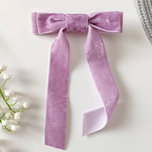 May include: A large lavender velvet bow with long tails. The bow is tied in a classic style with the tails hanging down.