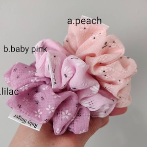 Puede incluir: Tres scrunchies en colores melocotón, rosa bebé y lila con un patrón floral. Los scrunchies están hechos de tela suave y tienen una pequeña etiqueta que dice "Ruby Stripe".