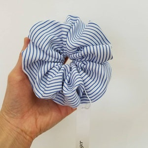 May include: A blue and white striped scrunchie made of fabric. The scrunchie is in the shape of a circle and is being held by a hand.
